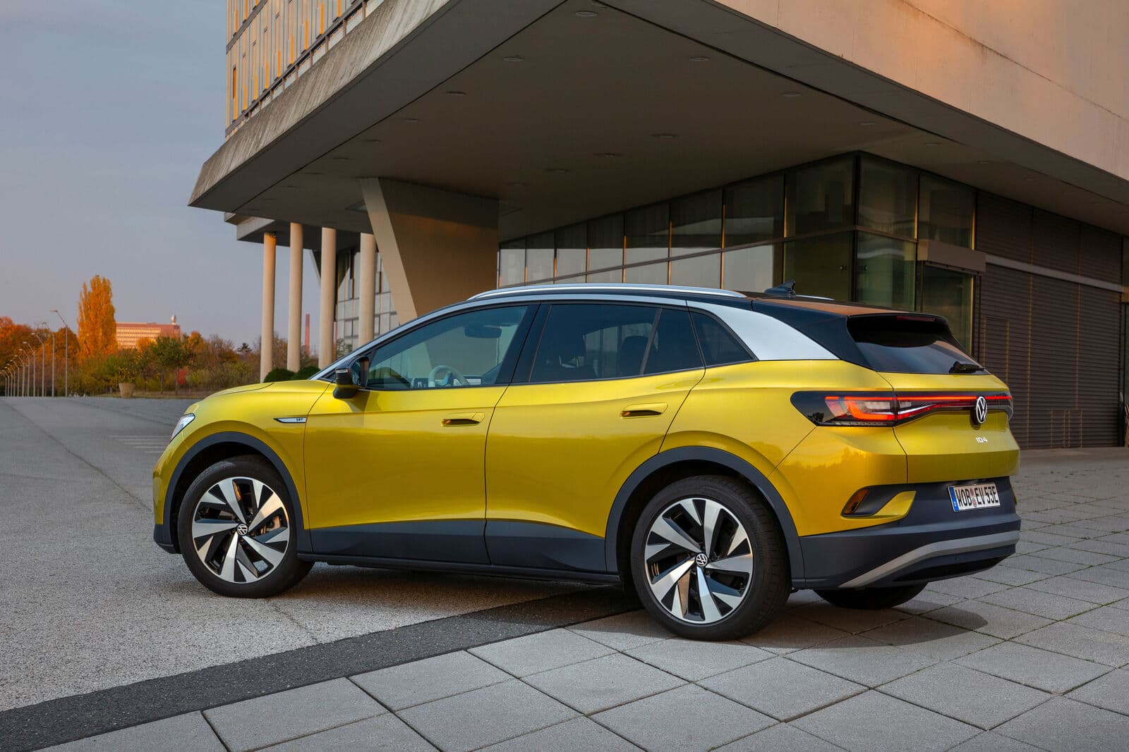Yellow Volkswagen ID.4 electric SUV parked beside a modern building at dusk, rear three-quarter view