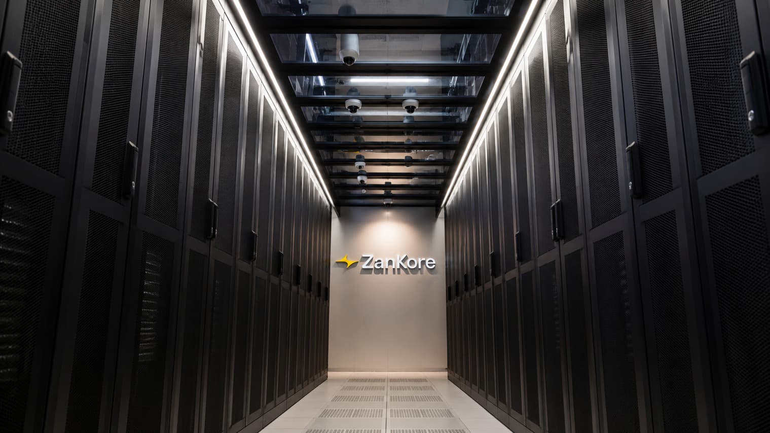 Rows of black server racks in a data hall with the ZanKore sign on the end wall, from the company's newsroom