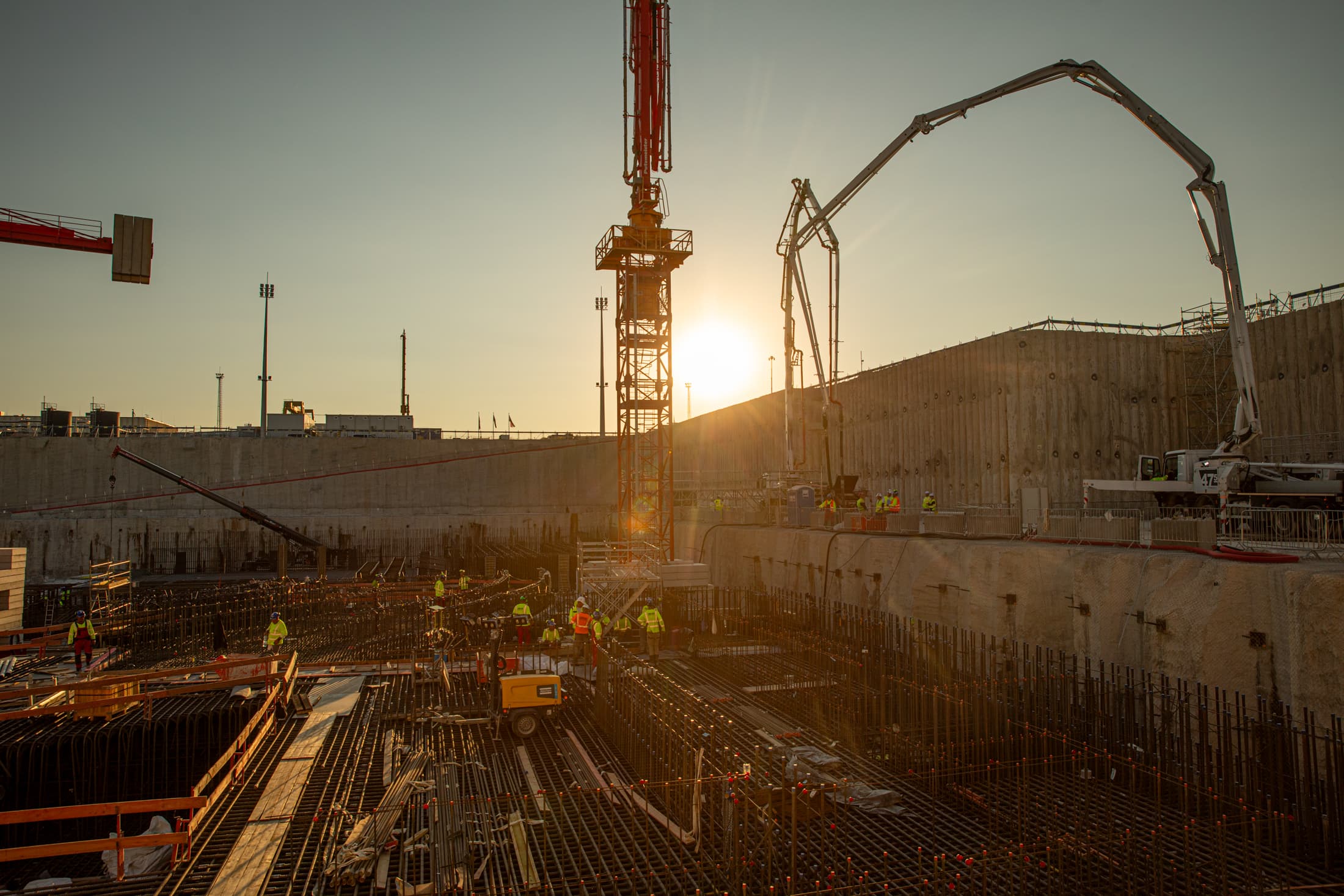 Paks II nuclear expansion construction site in Hungary, with workers, a tower crane and a concrete pump at sunset
