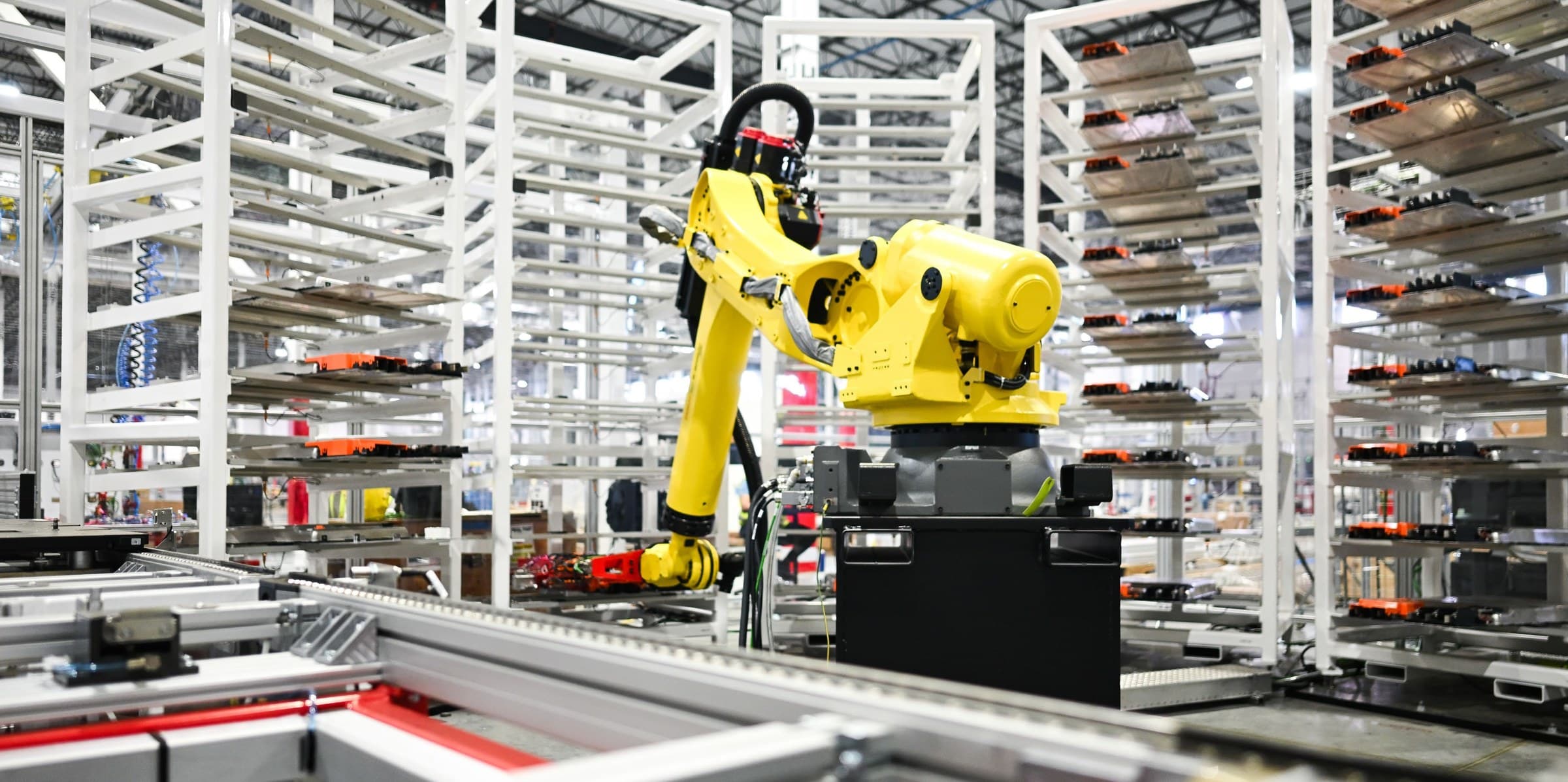 A yellow industrial robot arm beside racks of battery components on a Tesla production line