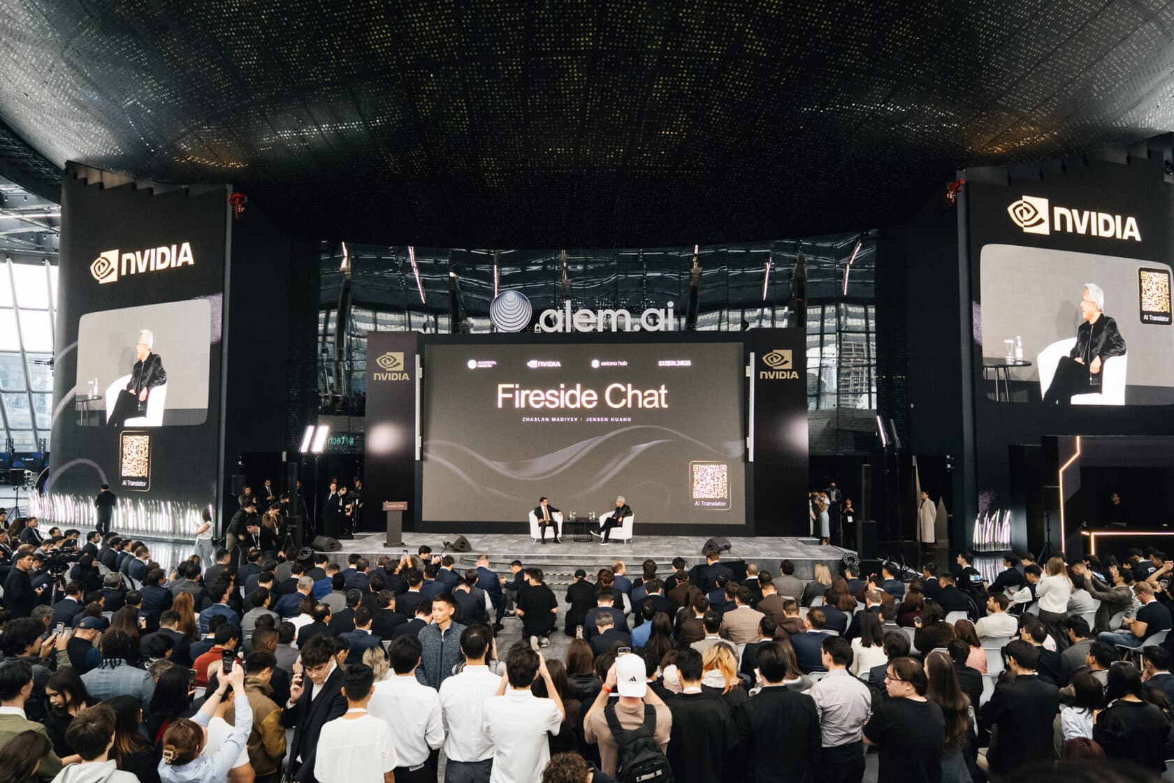 NVIDIA CEO Jensen Huang on stage in a fireside chat before a crowd in Astana, Kazakhstan, beneath NVIDIA signs