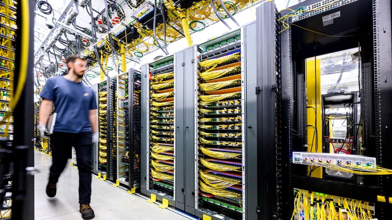 Data center employee walking past server racks with yellow cabling in an Amazon data center