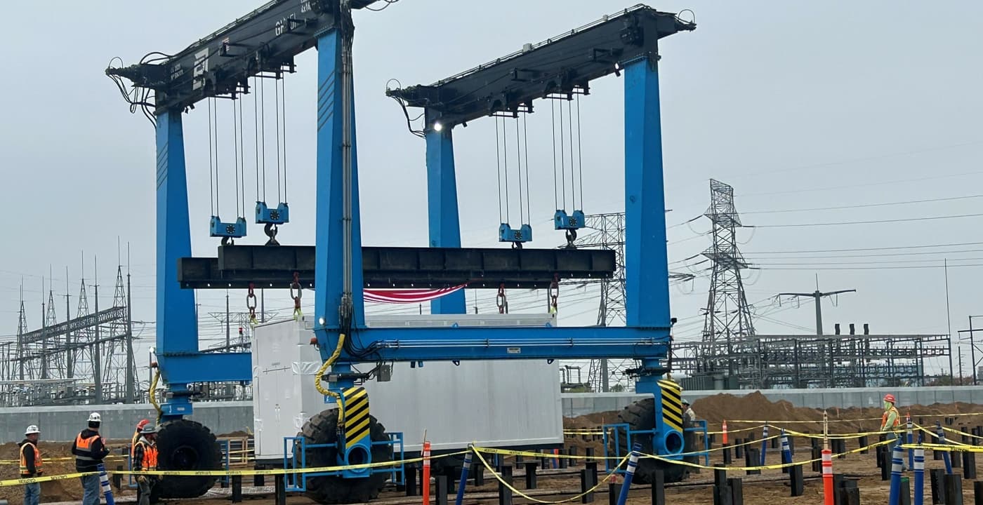 Blue gantry crane lifting a white battery unit at a substation construction site, from Xcel Energy's newsroom