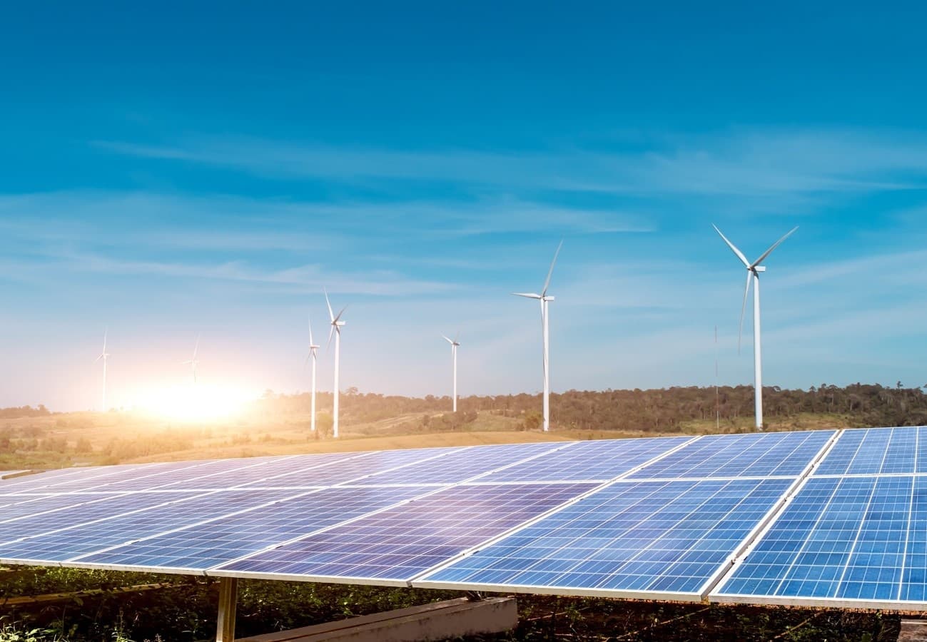 Solar panels in the foreground with wind turbines on a hillside under a blue sky, an illustrative image from Blueleaf Energy's website