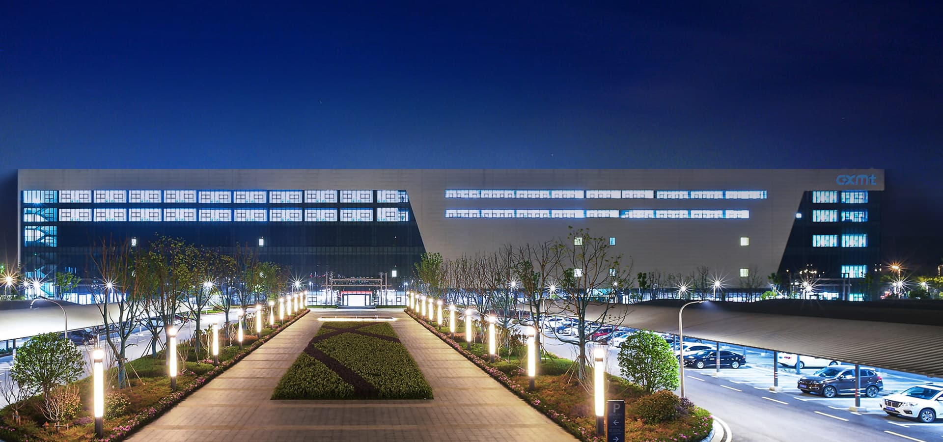Night view of a CXMT DRAM manufacturing facility with the CXMT logo on its facade and a lit walkway in front