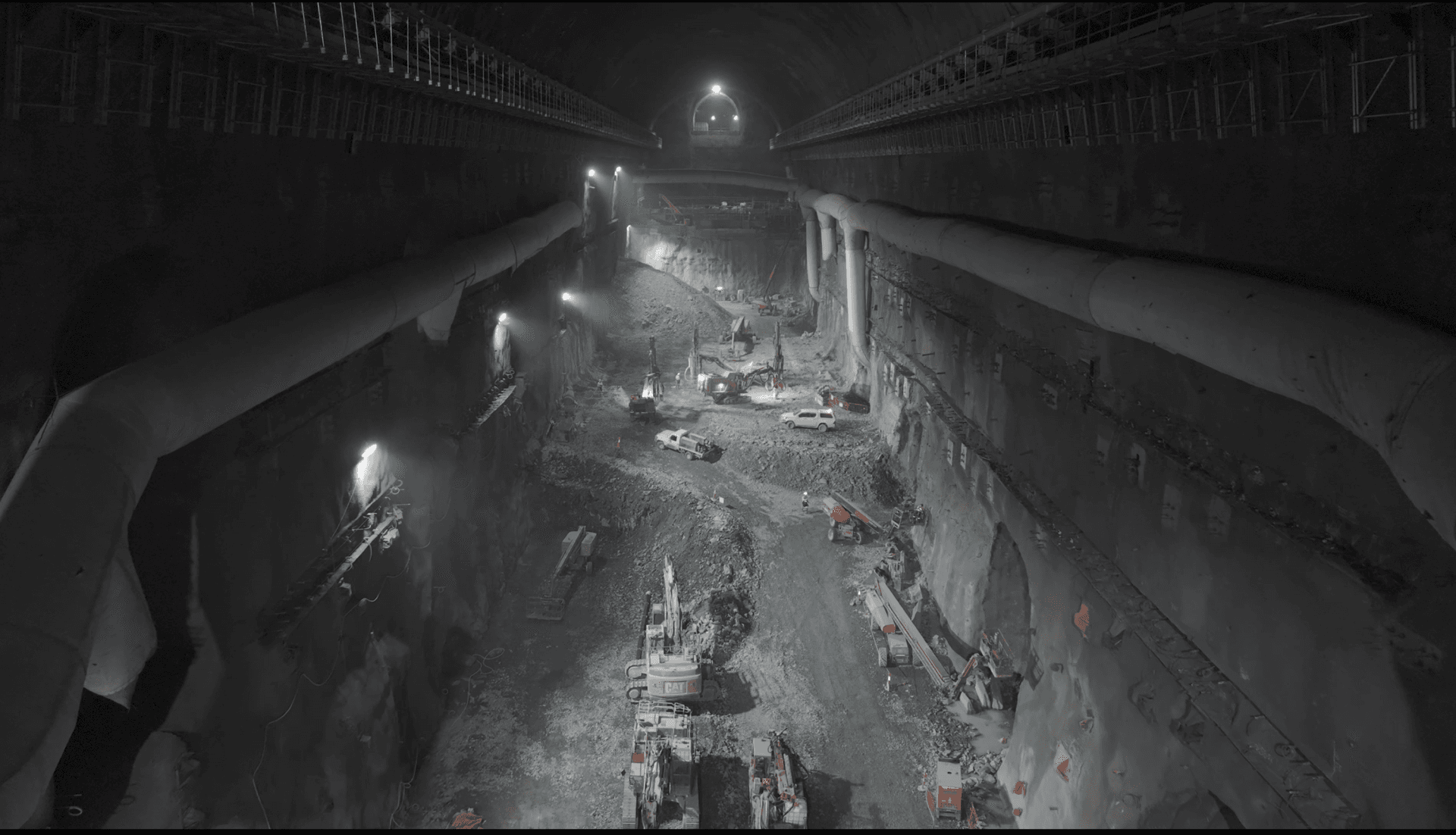 Excavators and drill rigs working in the underground machine hall of the Snowy 2.0 pumped hydro project, aerial view