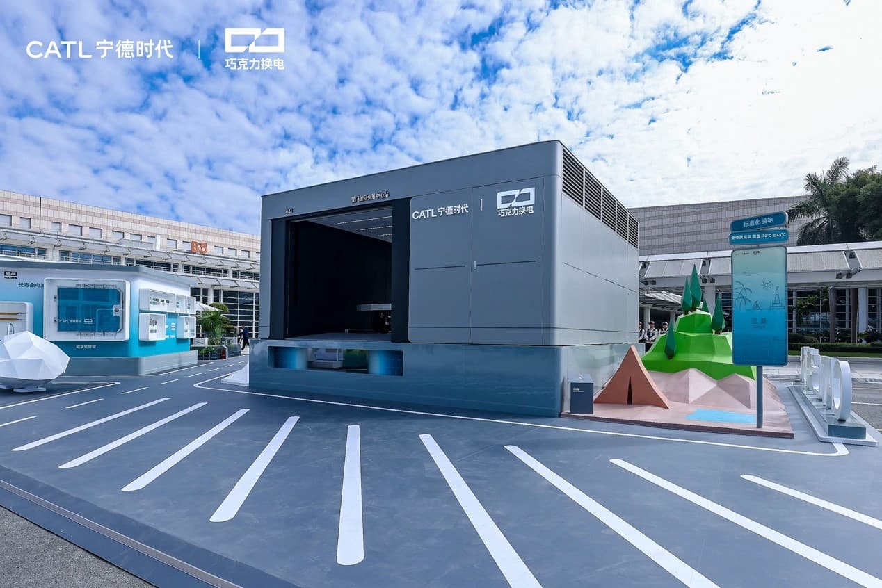 A grey CATL Choco-Swap battery swap station with an open drive-in bay on a paved forecourt under a cloudy blue sky