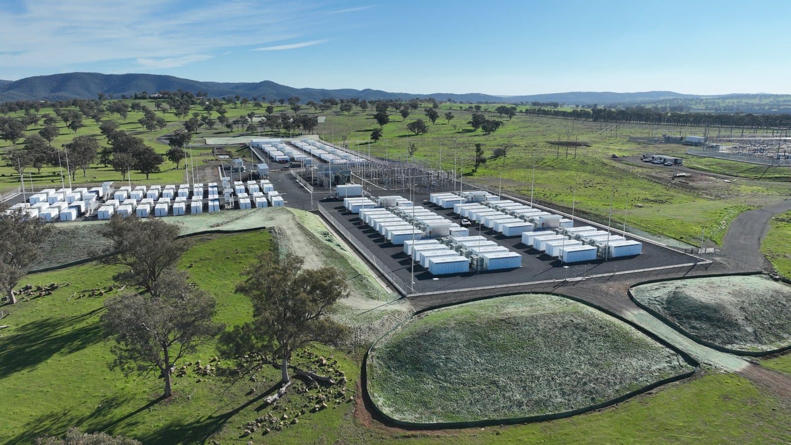 Aerial view of rows of white battery containers and a substation at an Akaysha Energy site in green Australian hills.