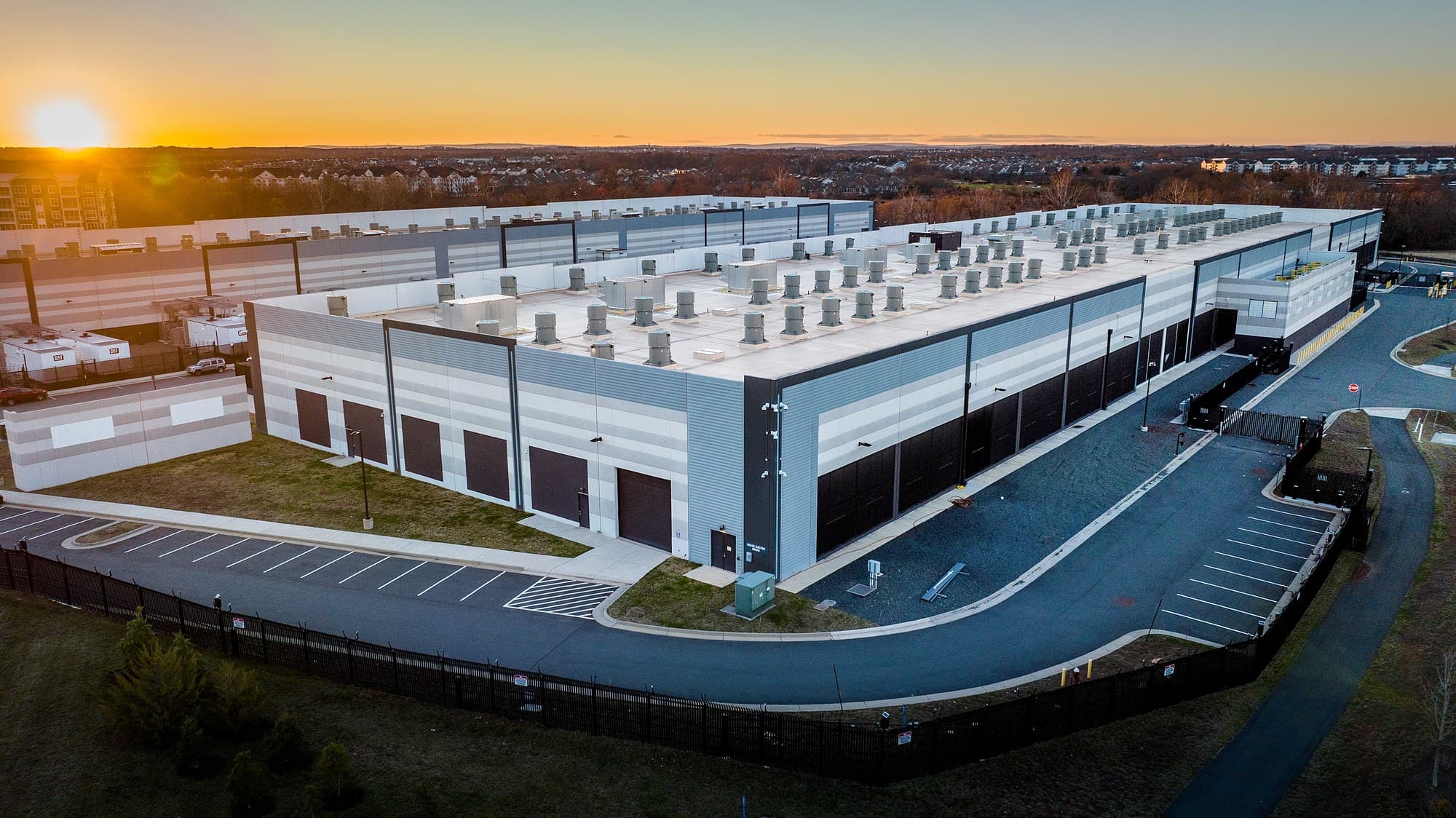 Aerial view at sunset of a large Amazon Web Services data center building with rooftop air handlers