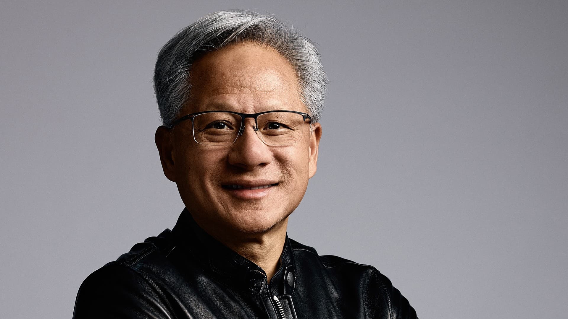 Official NVIDIA portrait of CEO Jensen Huang in a black leather jacket against a grey studio background