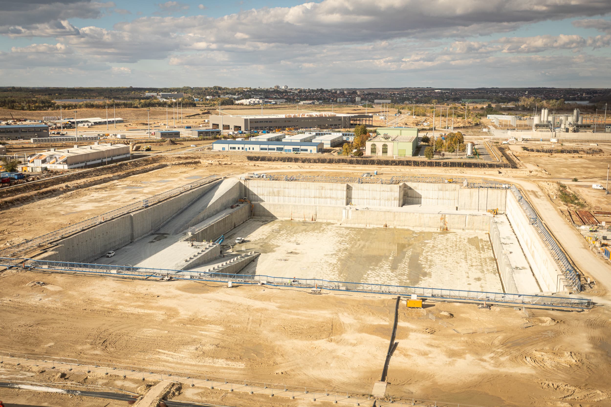 Excavated foundation pit at the Paks II nuclear expansion construction site in Hungary, with site buildings behind